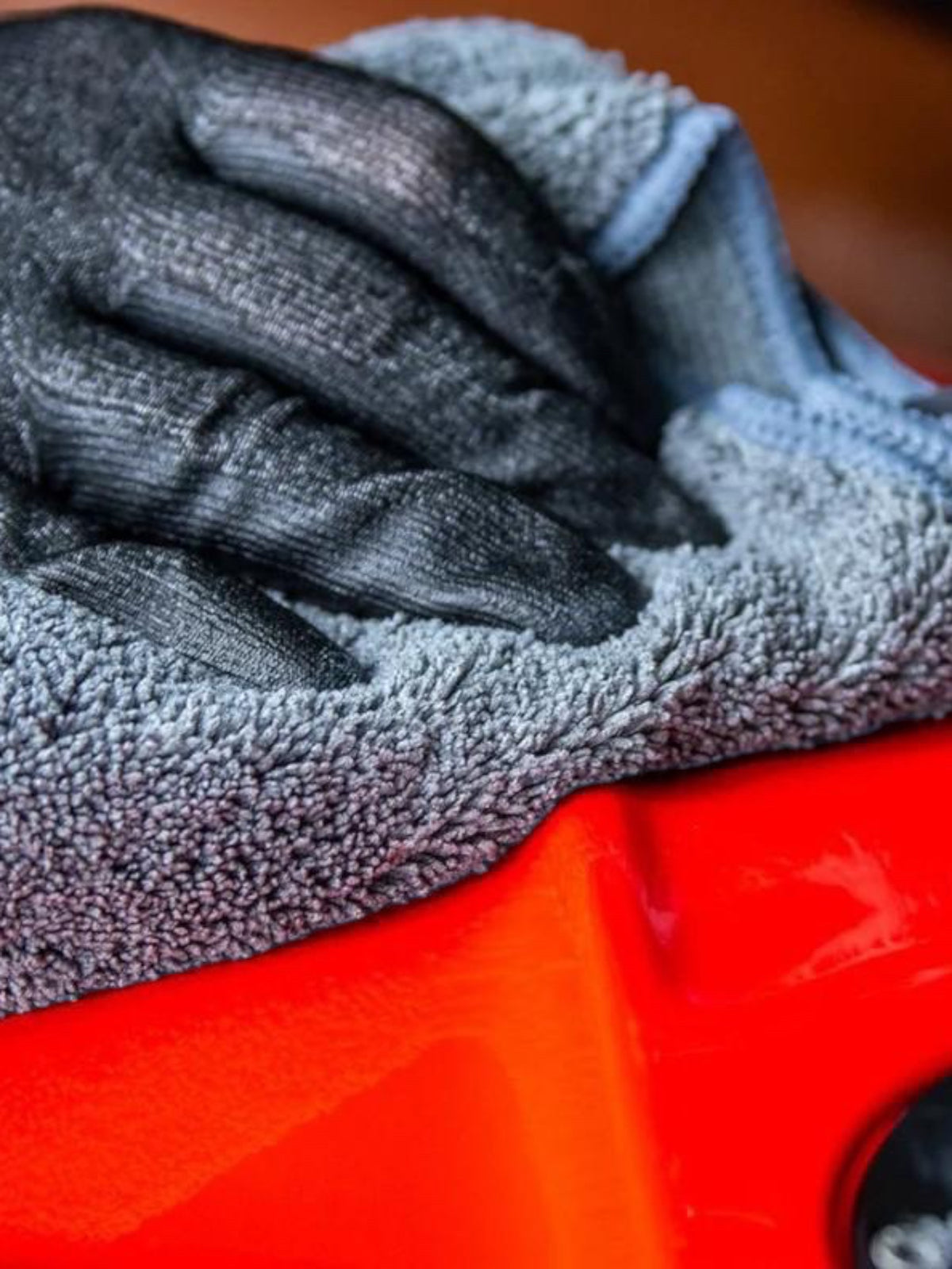 Baffle Haus Muc Off grey microfibre polishing cloth cleaning a glossy red motorcycle surface with a gloved hand