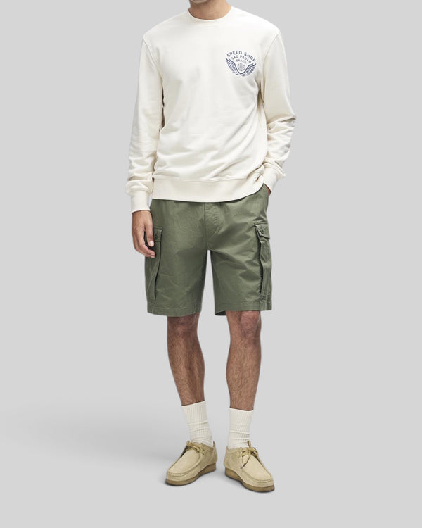 Baffle Haus Munificence crew fleece in dirty white with chest graphic, worn with olive cargo shorts and suede shoes.