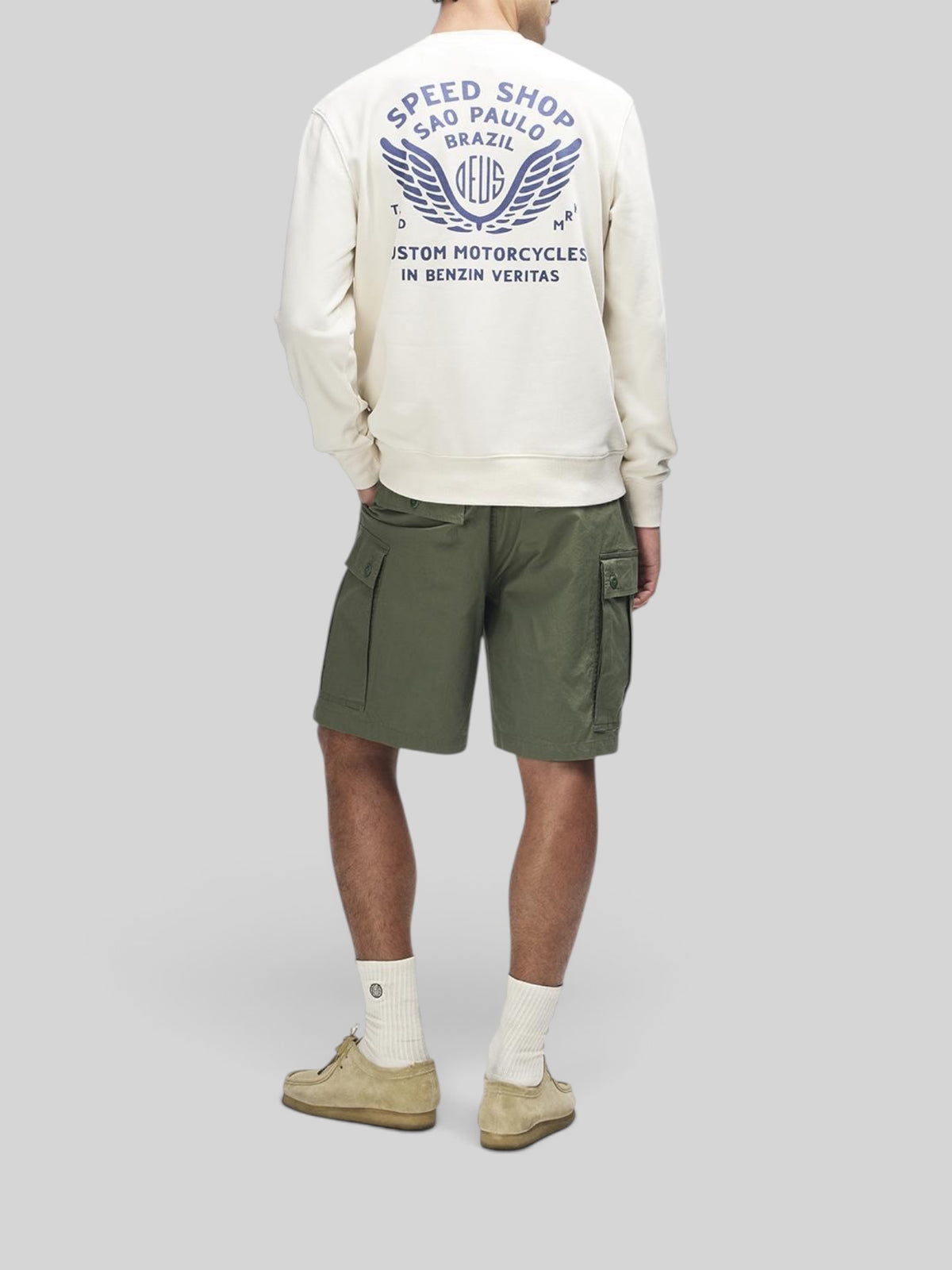 Baffle Haus Munificence crew fleece in dirty white with blue graphic print on back, worn with olive cargo shorts.