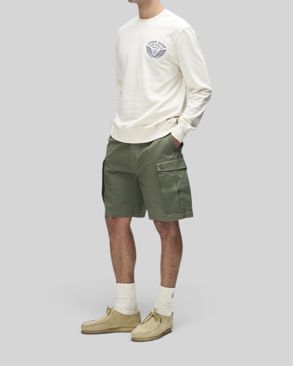 Baffle Haus Munificence crew fleece in dirty white with chest graphic, worn with olive cargo shorts and suede shoes.