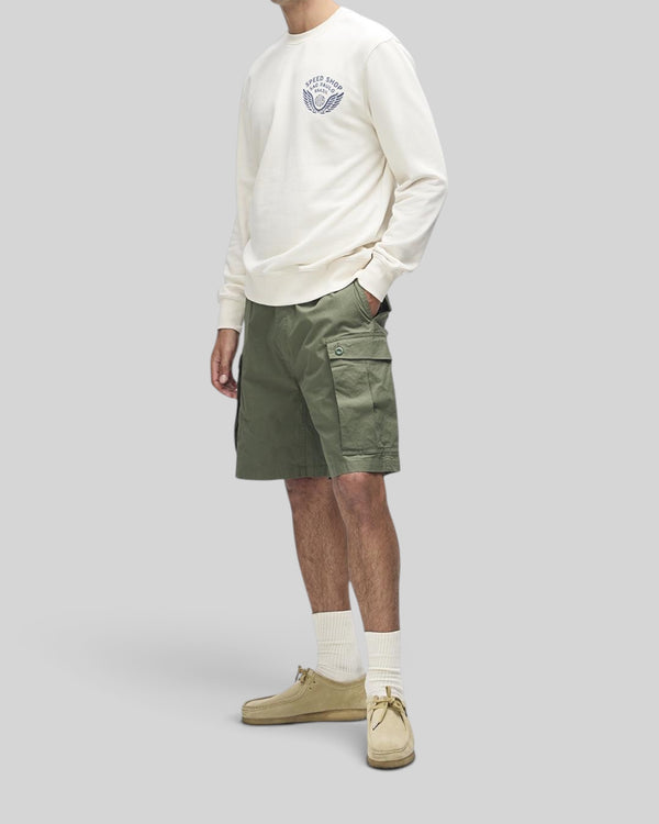 Baffle Haus Munificence crew fleece in dirty white with chest graphic, worn with olive cargo shorts and beige shoes.