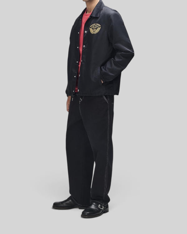 Baffle Haus Munificence nylon coach jacket in black with chest graphic, worn by a model with black trousers.