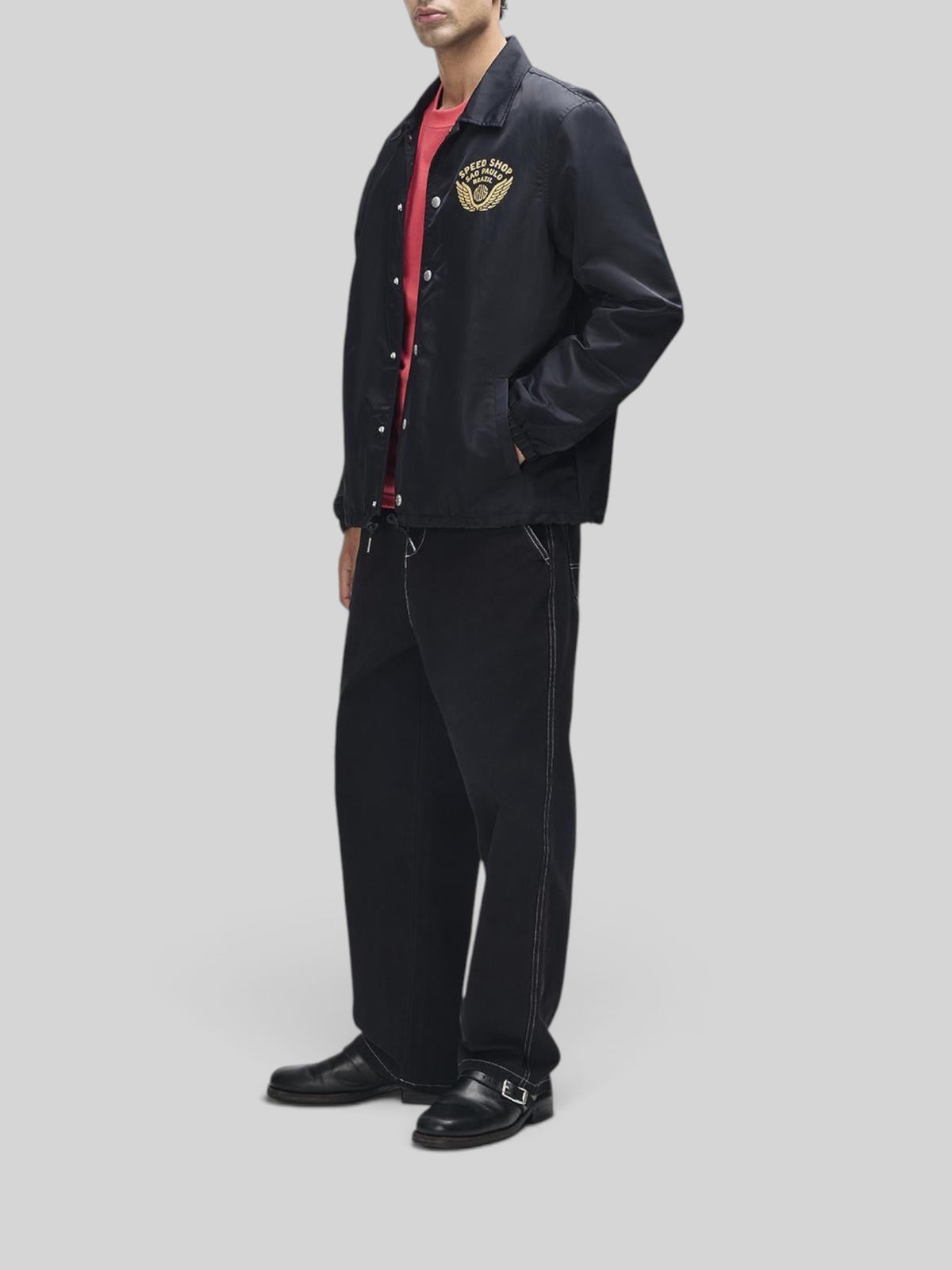 Baffle Haus Munificence nylon coach jacket in black with chest graphic, worn by a model with black trousers.