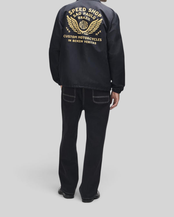 Baffle Haus Munificence nylon coach jacket in black with gold graphic print on back, worn by a man from behind.