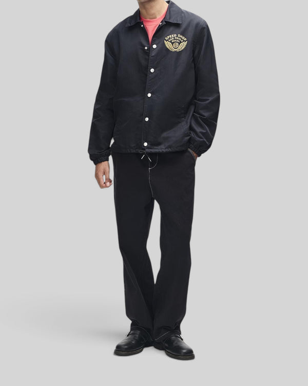 Baffle Haus Munificence nylon coach jacket in black with chest graphic, snap buttons, and regular fit on a model.