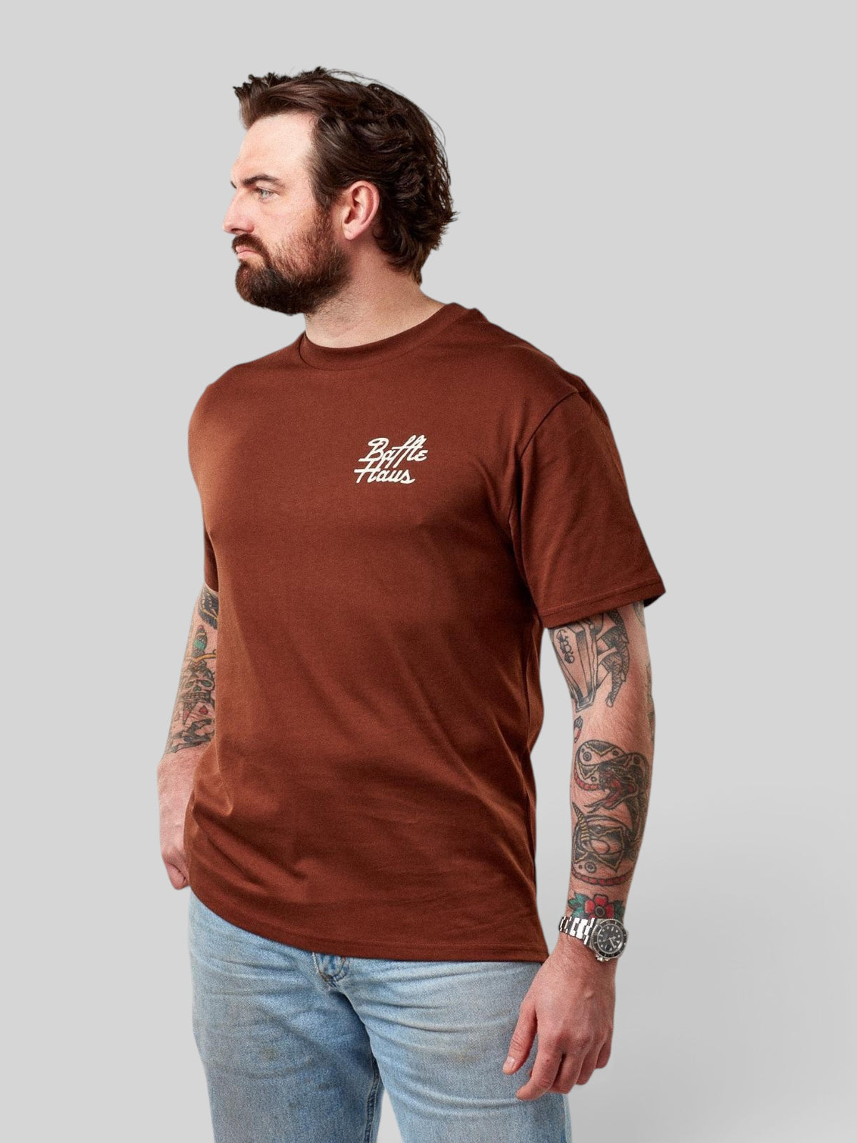 Baffle Haus Mustang Tee in cocoa brown cotton with white chest logo, worn by a bearded man in light blue jeans.