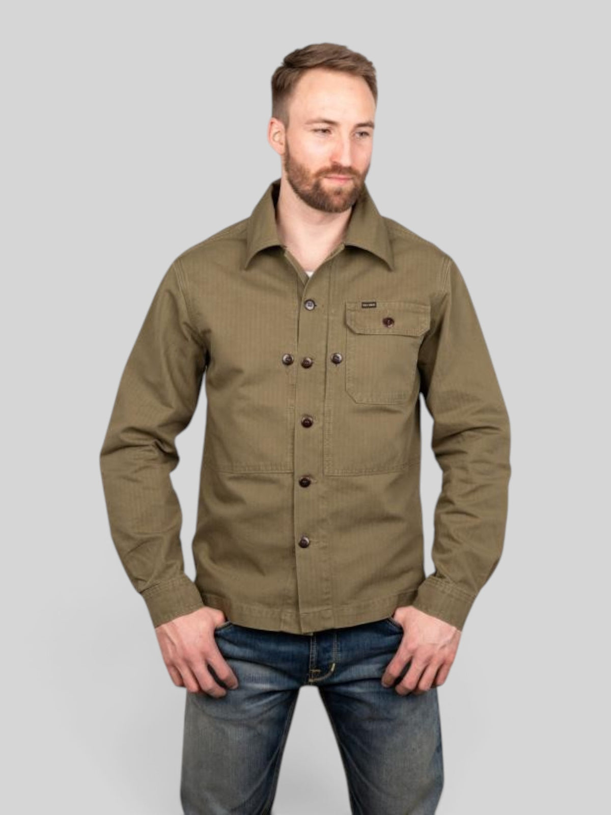 Baffle Haus 1967 Utility Shirt in olive herringbone twill cotton with chest pockets worn by a man in blue jeans