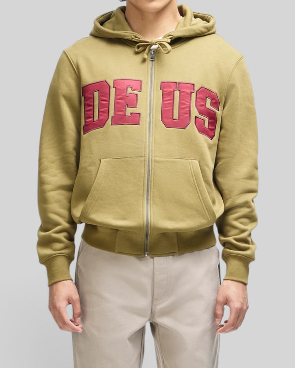 Baffle Haus olive green zip-up hoodie with red DEUS chest appliqué, kangaroo pocket, and ribbed cuffs on a model