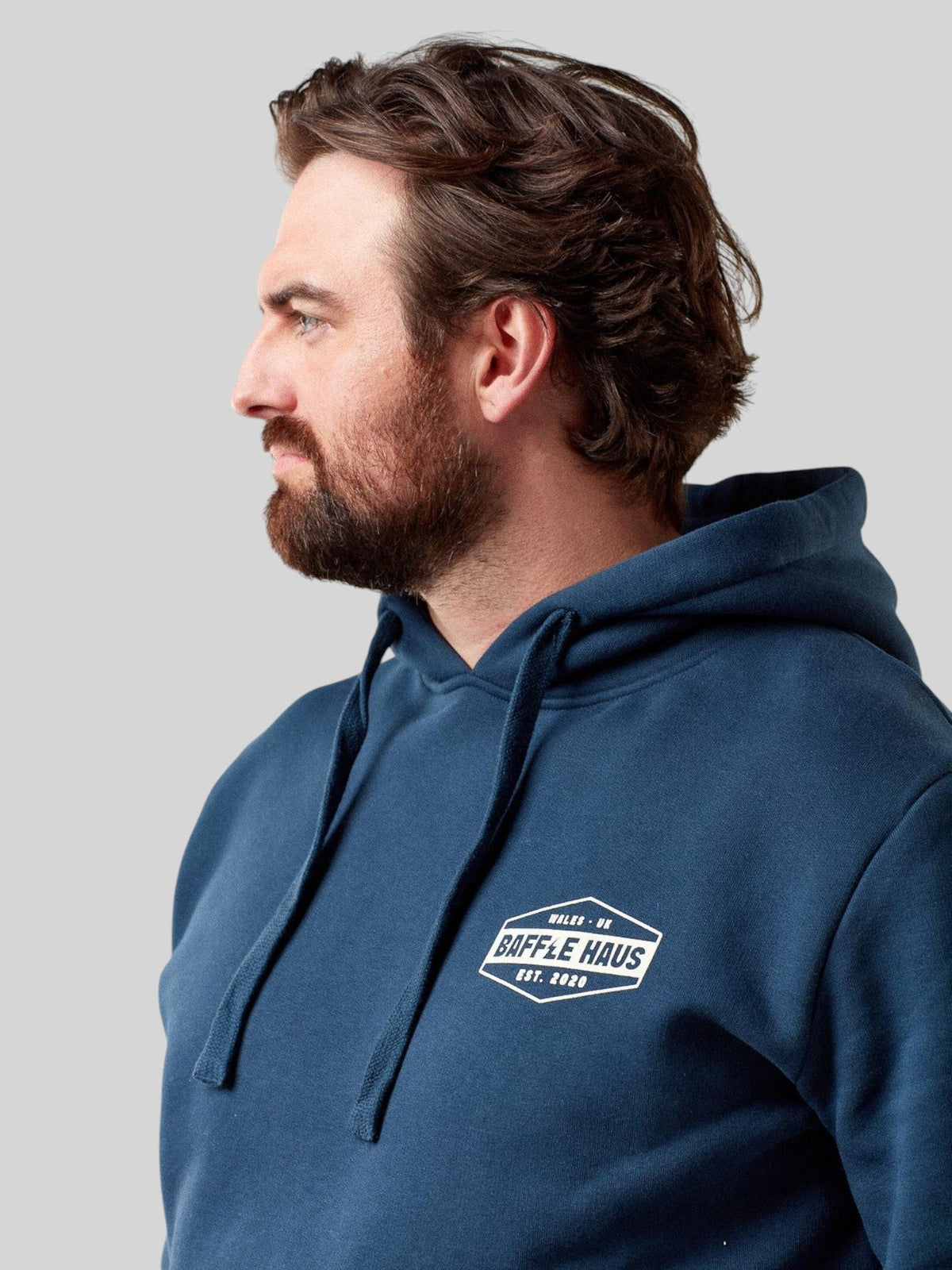 Baffle Haus retro hoodie in pageant blue with a white chest logo, worn by a man in a side profile view.