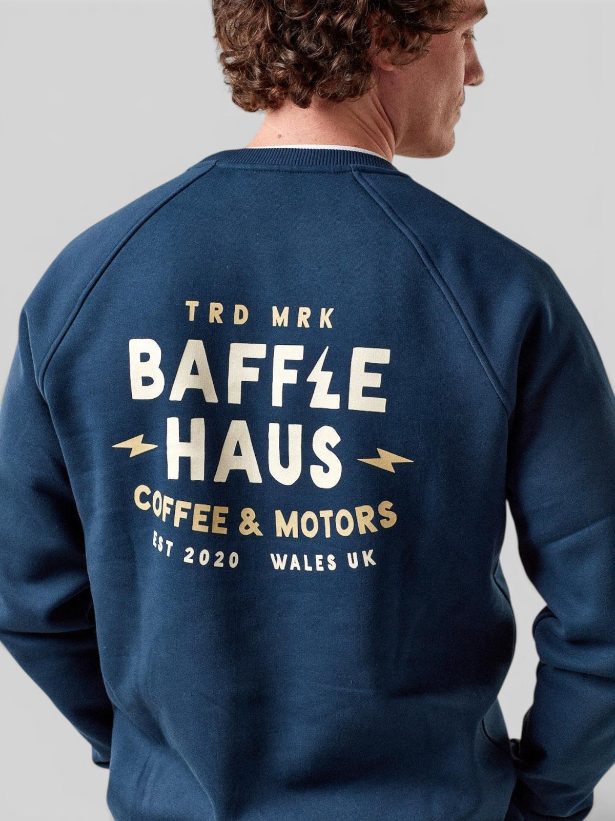 Baffle Haus Coffee & Motors sweatshirt in pageant blue with cream graphic print on the back, worn by a male model.