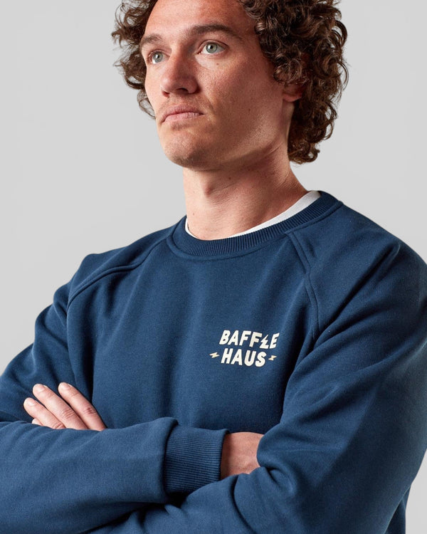 Baffle Haus Coffee & Motors sweatshirt in pageant blue with white chest logo, worn by a model with curly hair.