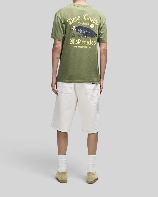 Baffle Haus Beep-Beep Tee in pine green with graphic print on back, worn with white shorts and beige shoes.