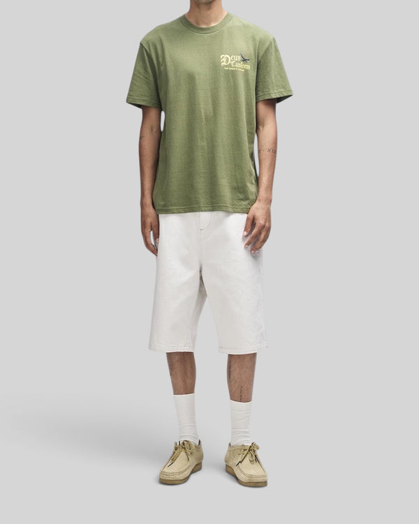 Baffle Haus Beep-Beep Tee in pine green with chest graphic, worn by a model with white shorts and tan shoes.