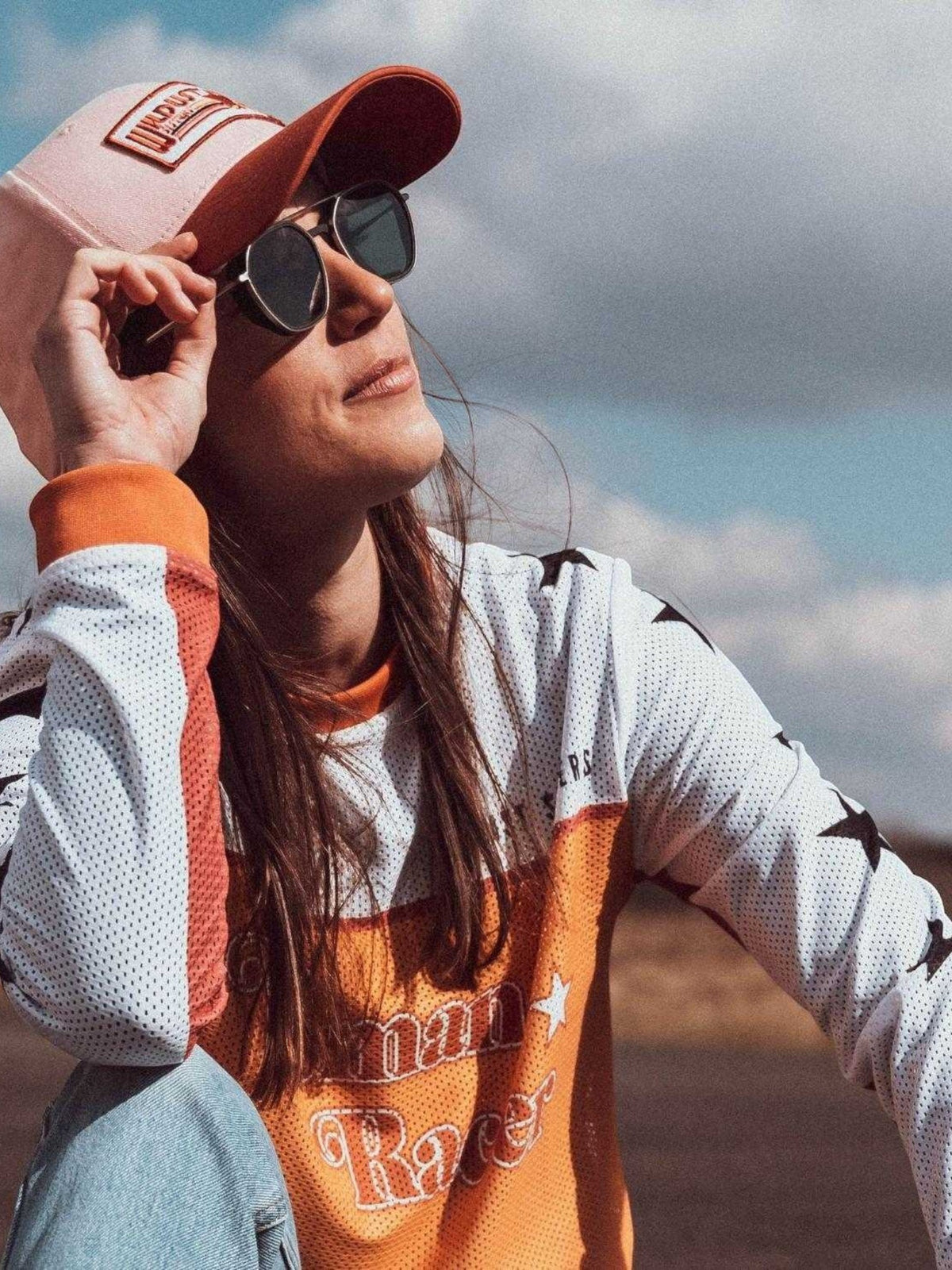 Baffle Haus woman wearing a pink and orange racer cap with a graphic patch, paired with a star-print jersey.