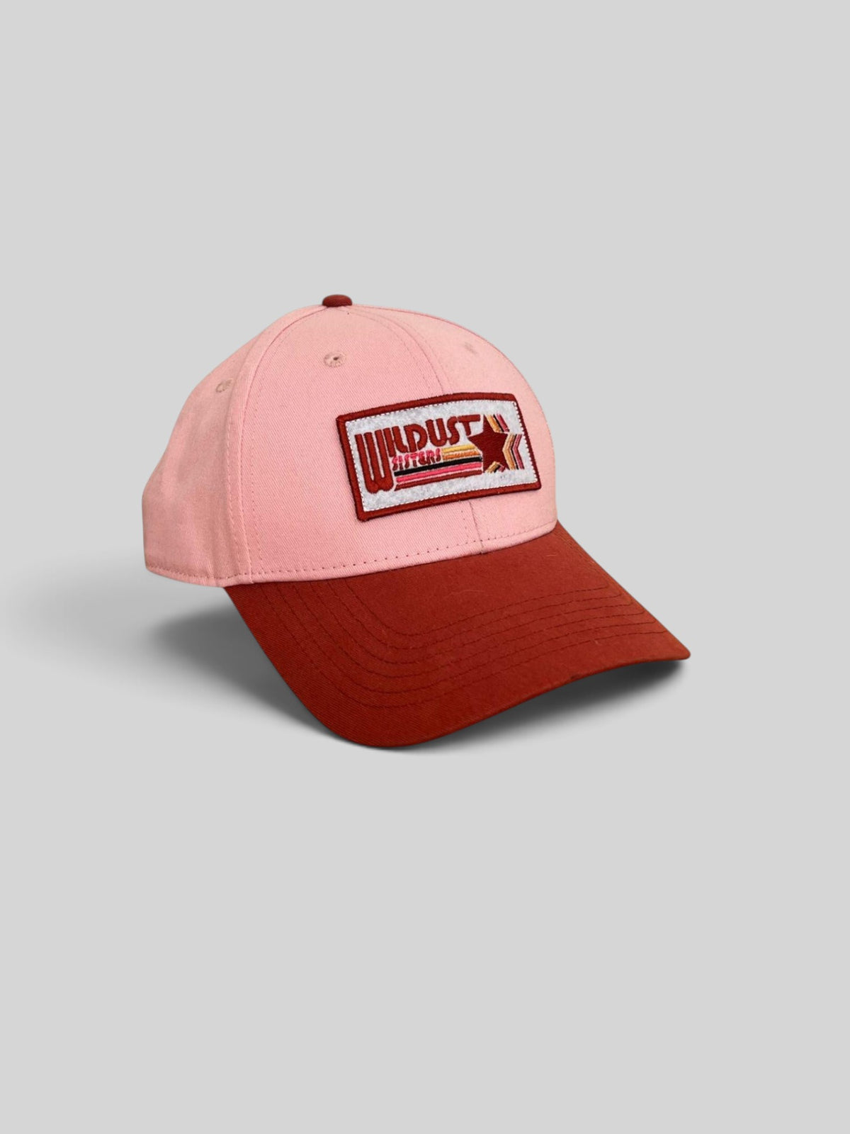 Baffle Haus woman racer cap in light pink with a dark red brim and a vintage-style Wildust Sisters embroidered patch.