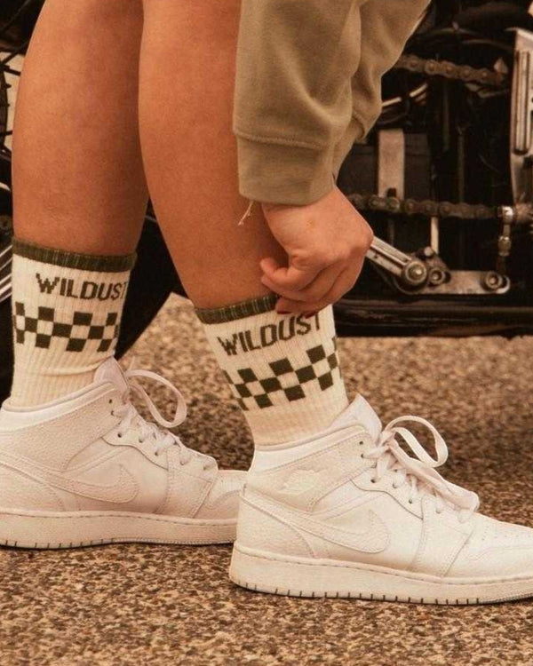 Baffle Haus race green and ecru socks with a checkered pattern and Wildust branding worn with white high-top sneakers