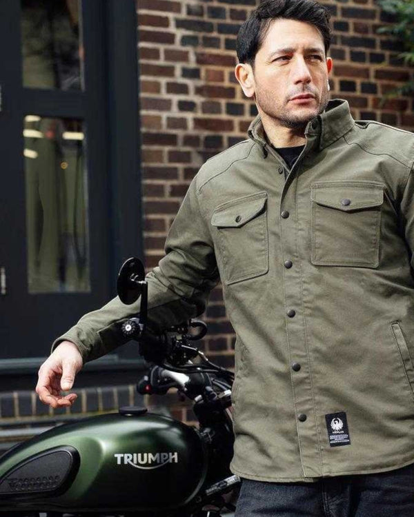 Baffle Haus Renegade riding shirt in green Cordura fabric with chest pockets, worn by a man next to a motorcycle.