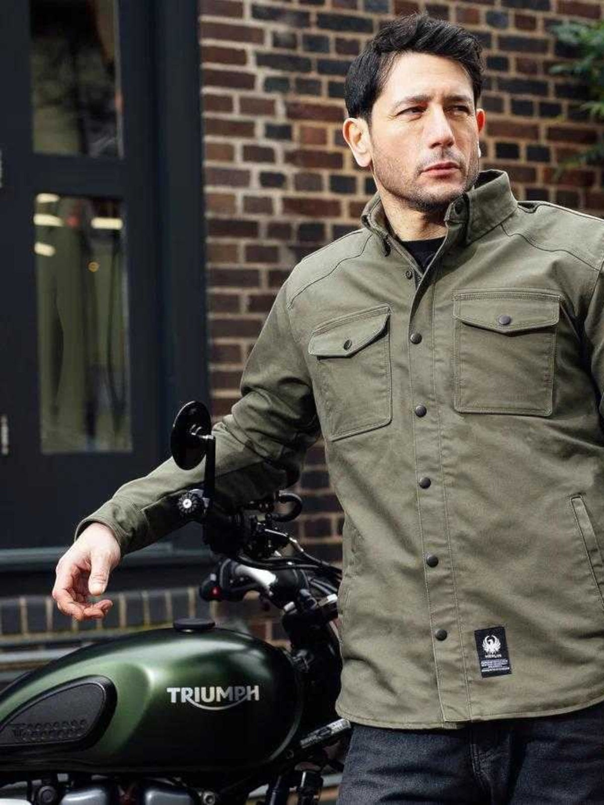 Baffle Haus Renegade riding shirt in green Cordura fabric with chest pockets, worn by a man next to a motorcycle.