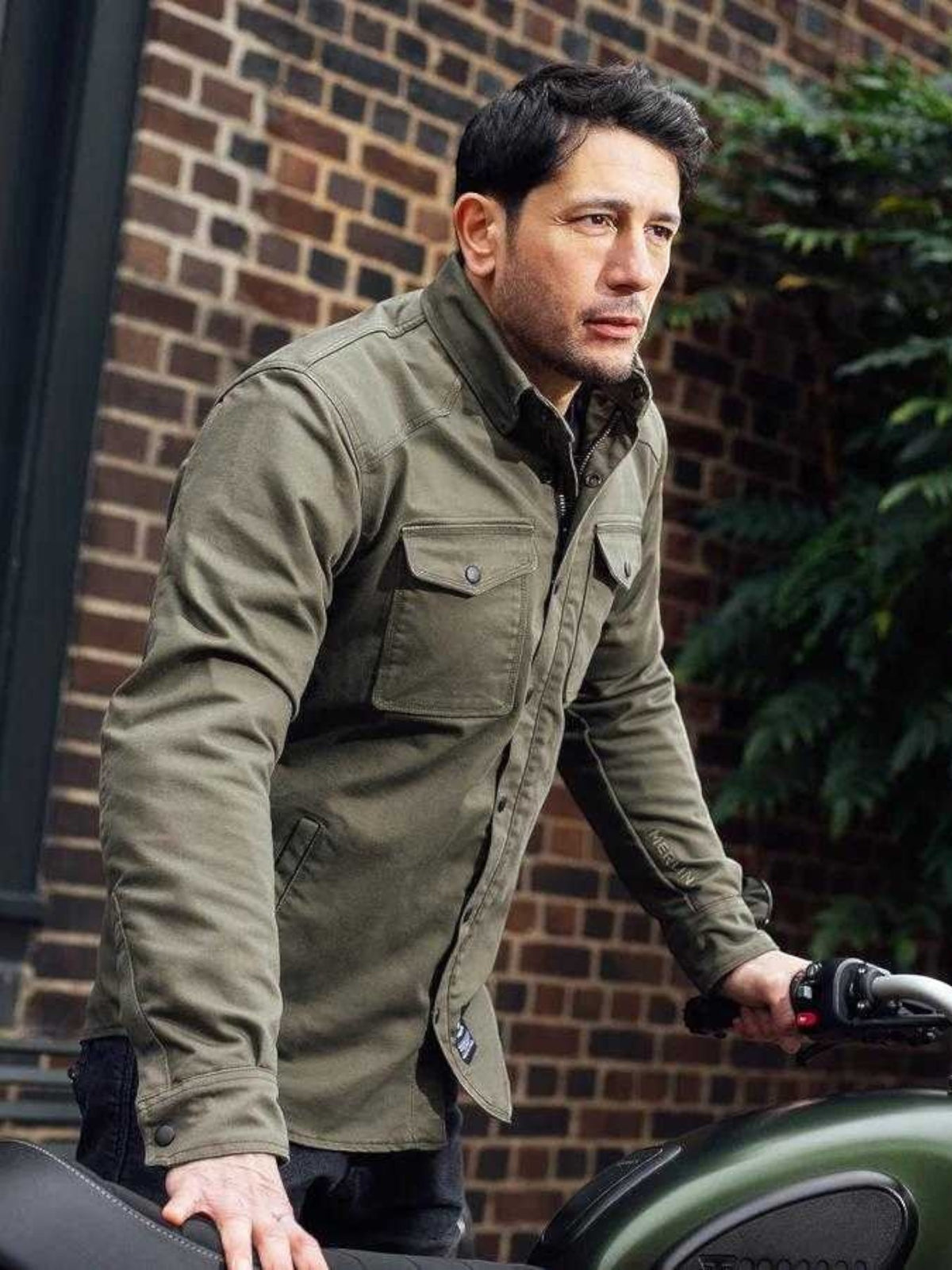 Baffle Haus Renegade green Cordura riding shirt with protective armour worn by a man standing next to a motorcycle