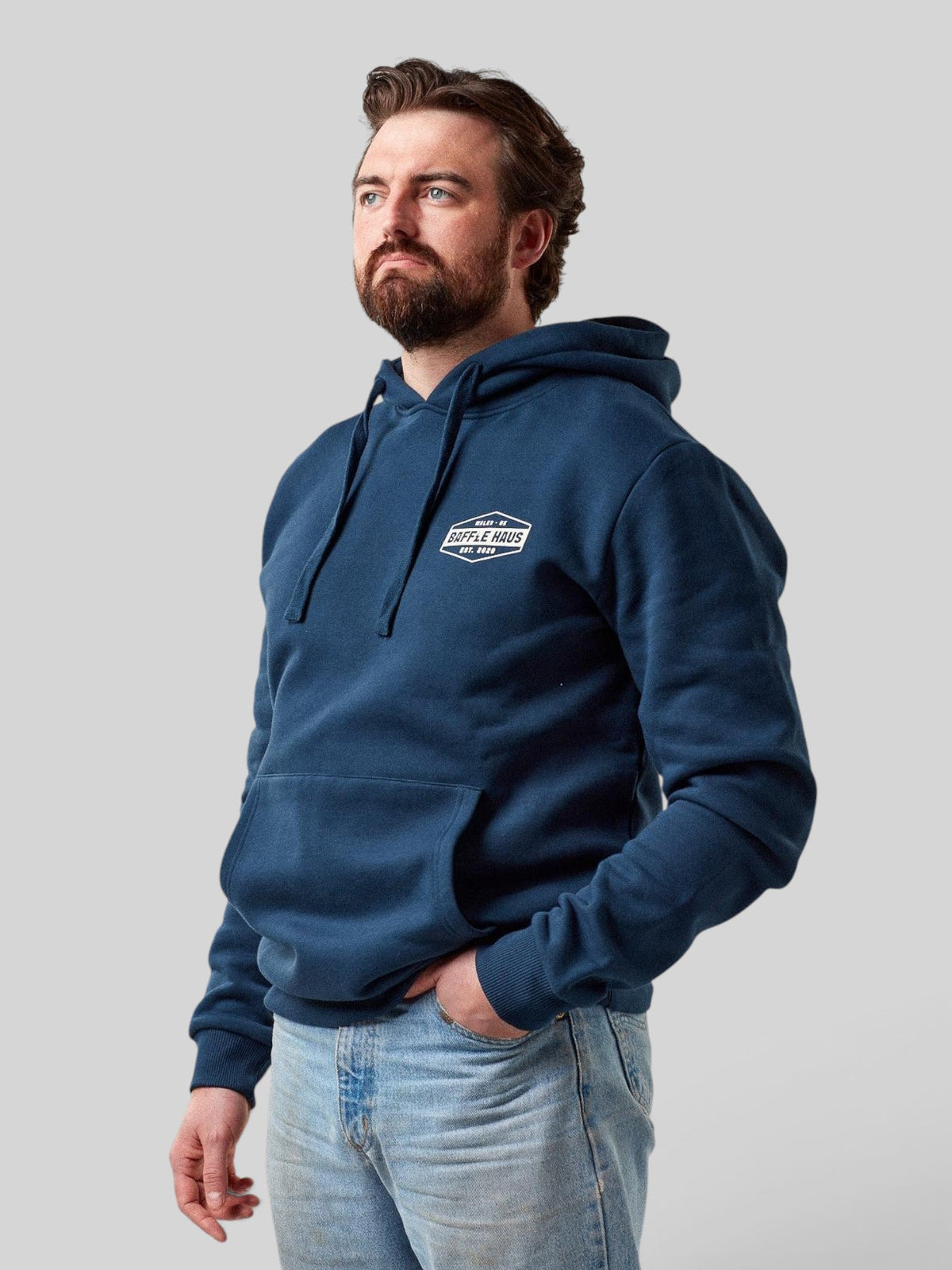 Baffle Haus retro hoodie in pageant blue with a chest logo, worn by a bearded man against a light grey background.