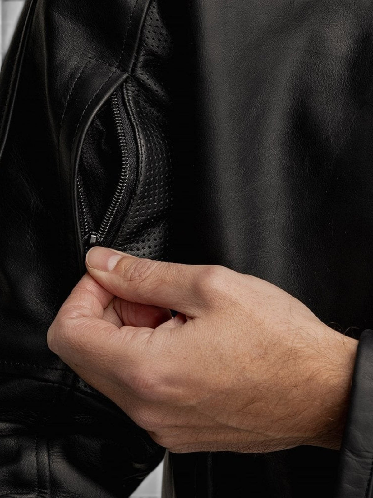 Close-up of a hand opening a zippered vent on a black Baffle Haus Motone Revolver cowhide leather riding jacket.