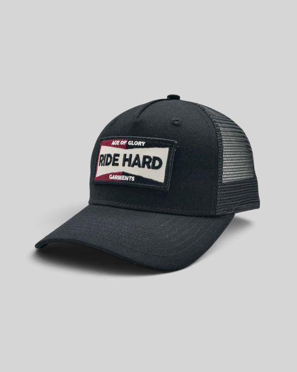 Baffle Haus Ride Hard black trucker cap with mesh back, snapback closure, and vintage-style embroidered patch.