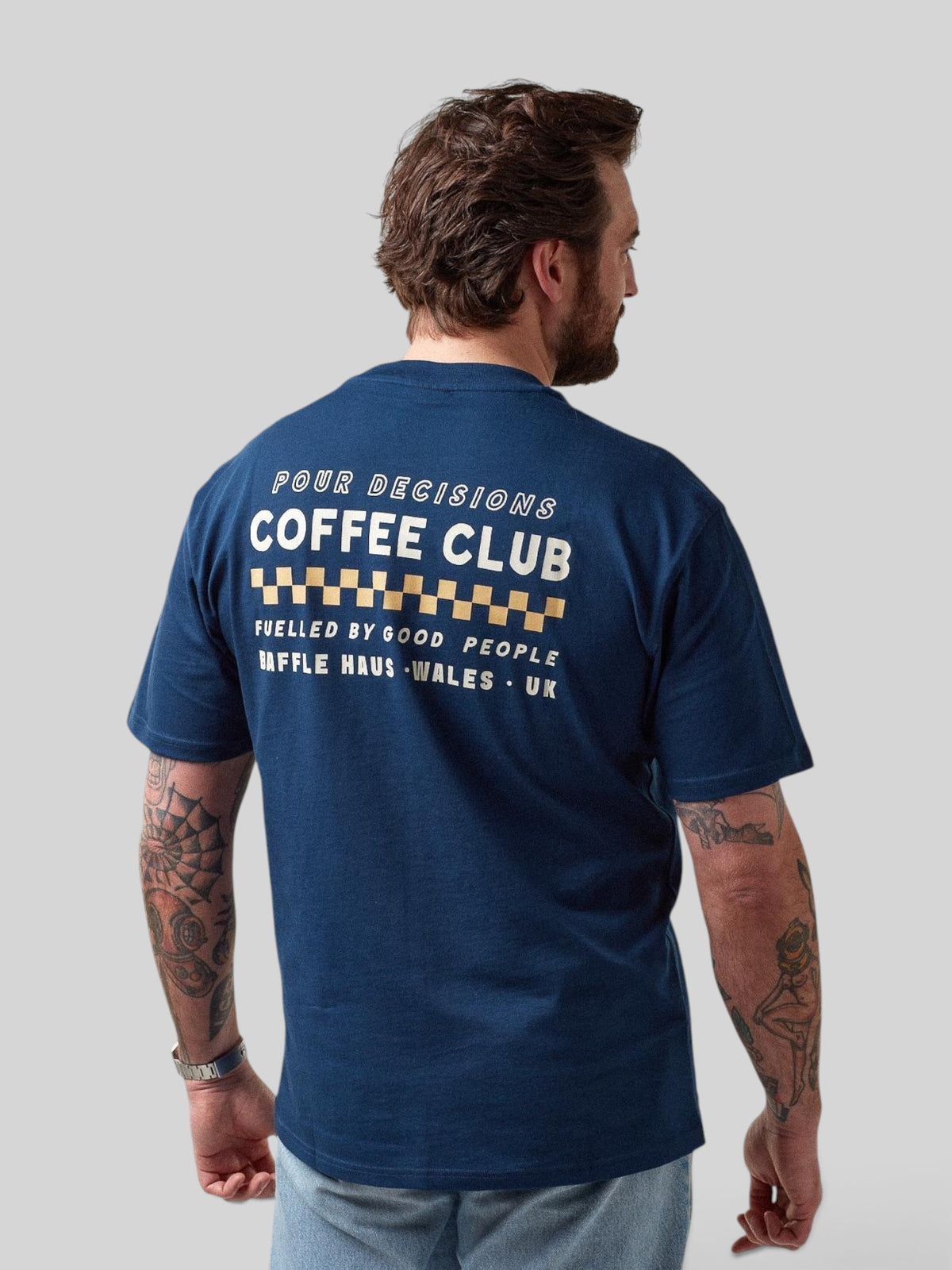 Back view of a man wearing a Baffle Haus royal navy cotton t-shirt with a white and gold coffee club graphic print.