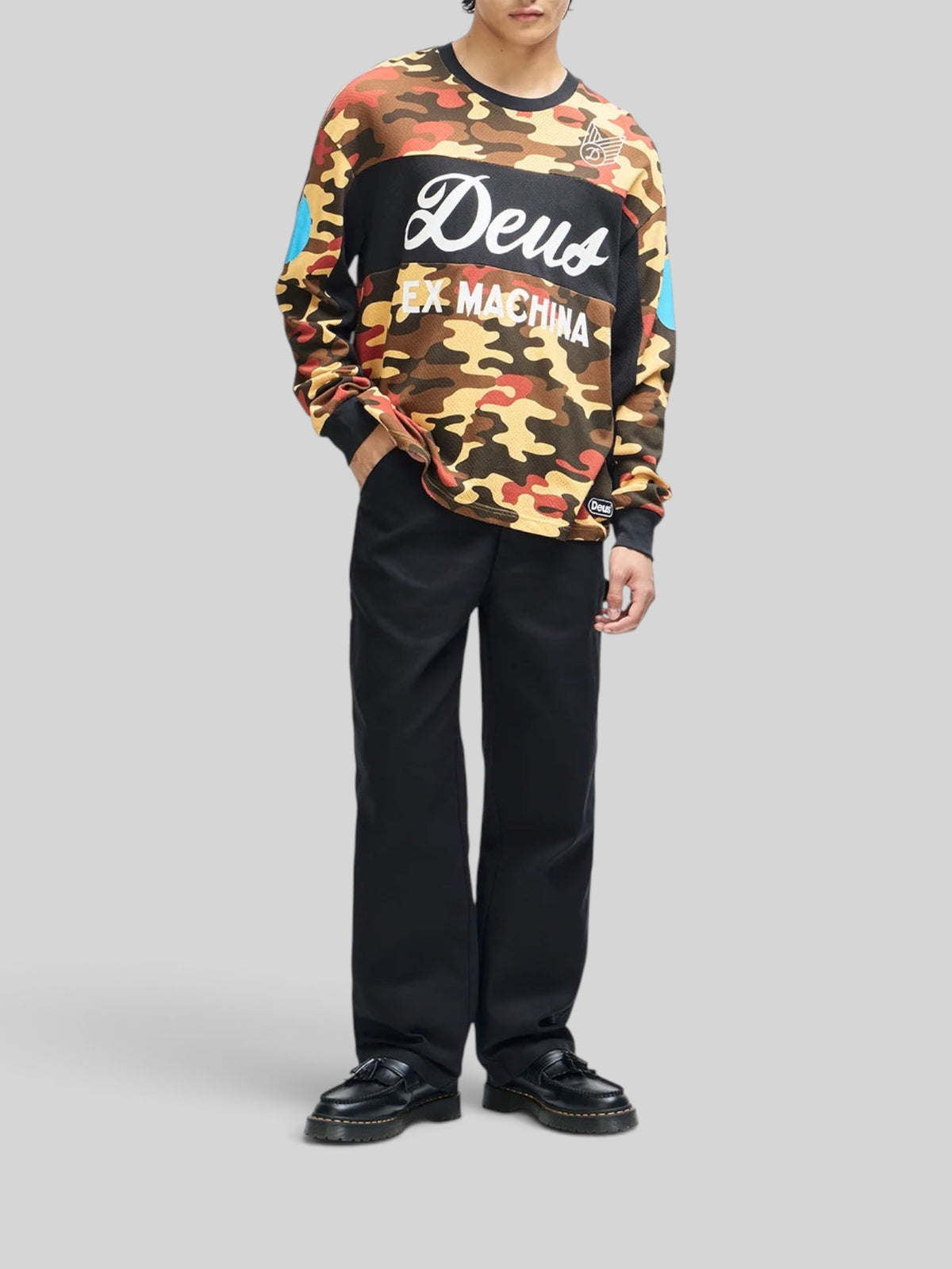Baffle Haus rust camo ombre moto jersey with graphic chest prints and loose fit, worn by a model with black trousers.