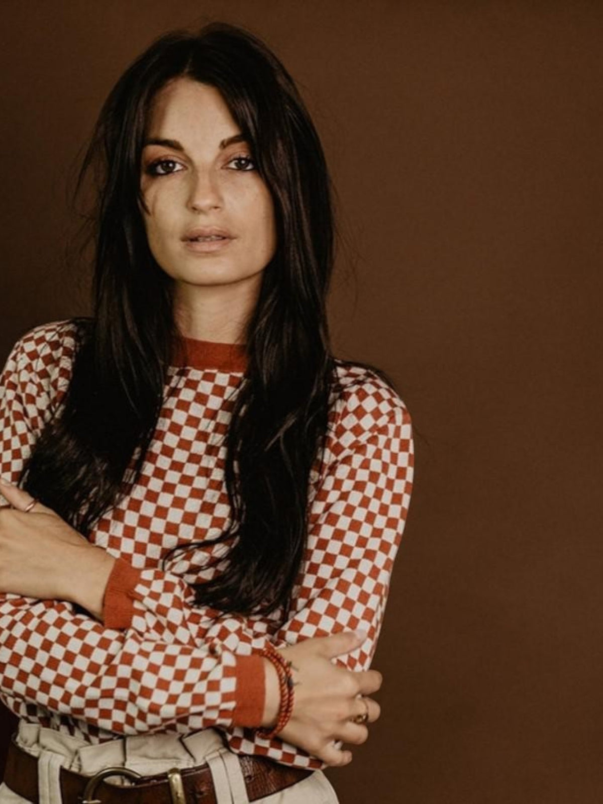 Baffle Haus rust and white chequered knit jumper with a mid-rise collar worn by a woman against a brown background