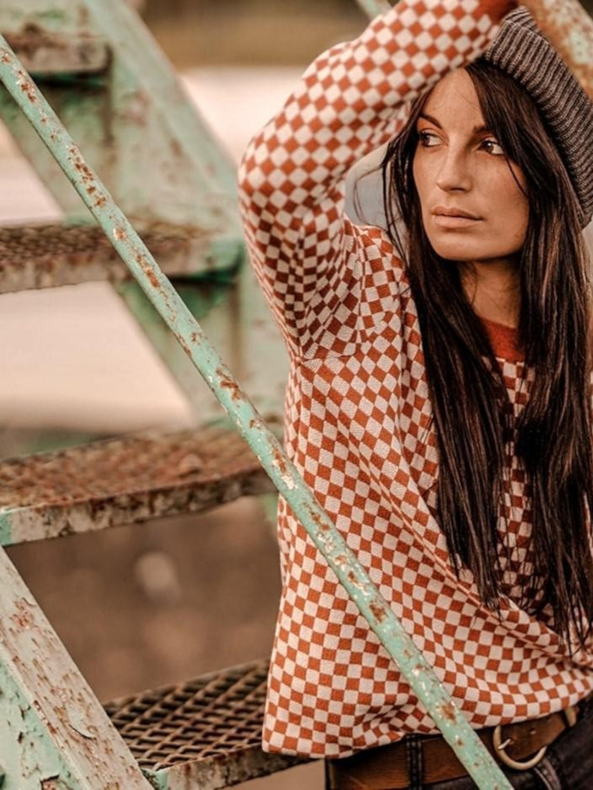 Baffle Haus rust and white chequered racing jumper worn by a woman with a beanie on a metal staircase