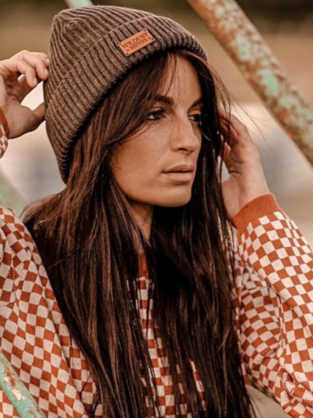 Baffle Haus woman wearing a rust and white chequered racing jumper and a brown ribbed beanie outdoors.