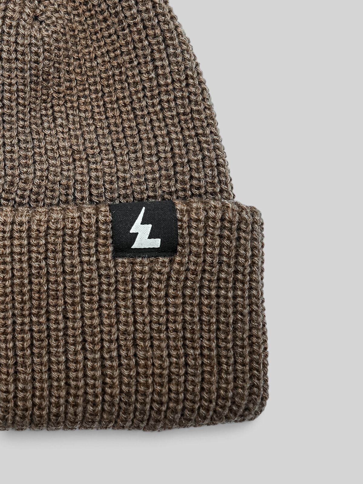 Baffle Haus sand coloured ribbed knit beanie with a woven logo patch on the folded cuff