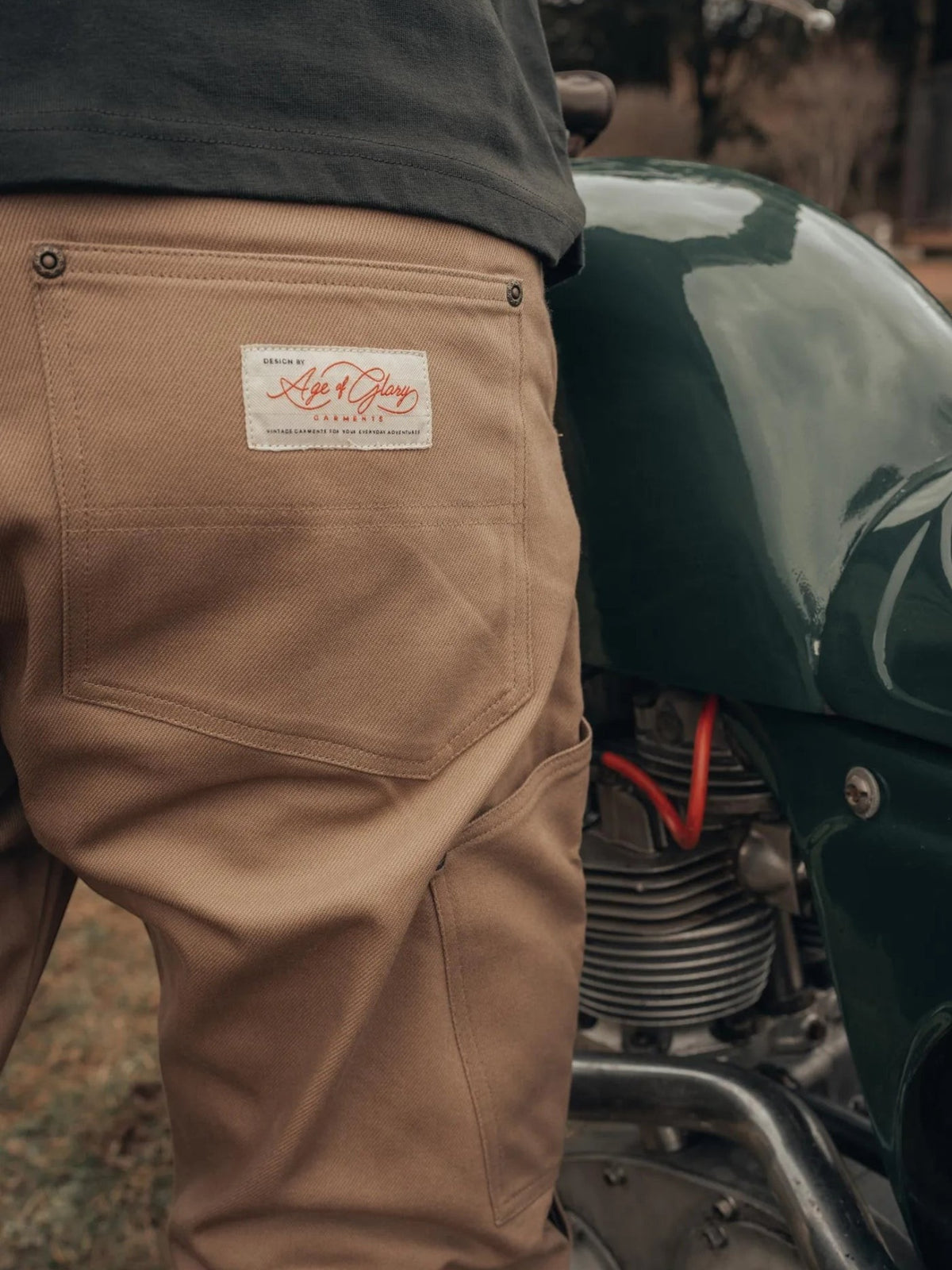 Baffle Haus Service Pants in desert khaki featuring a rear pocket with Age of Glory branding next to a motorcycle