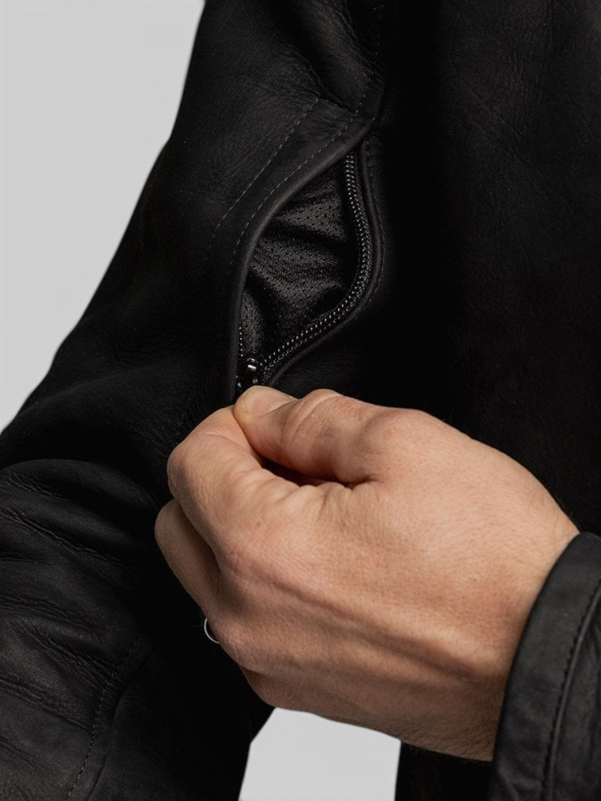 Close-up of a hand opening a zippered pocket on a black Baffle Haus Shōgun nubuck leather motorcycle jacket