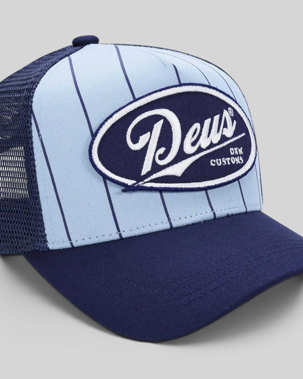 Baffle Haus Forecourt Trucker hat in sky blue with pinstripes, navy brim, and Deus Customs twill patch.