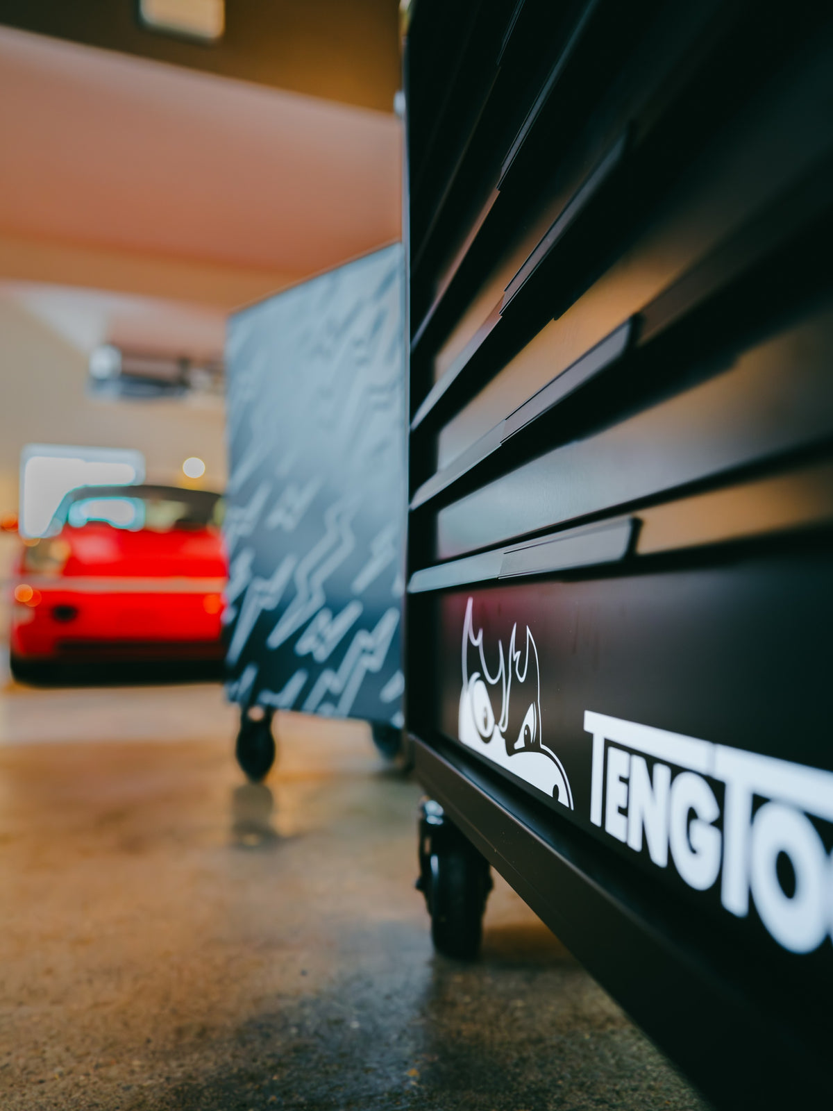 Baffle Haus black Teng tool box with branded logo in a garage setting with a blurred red car in the background