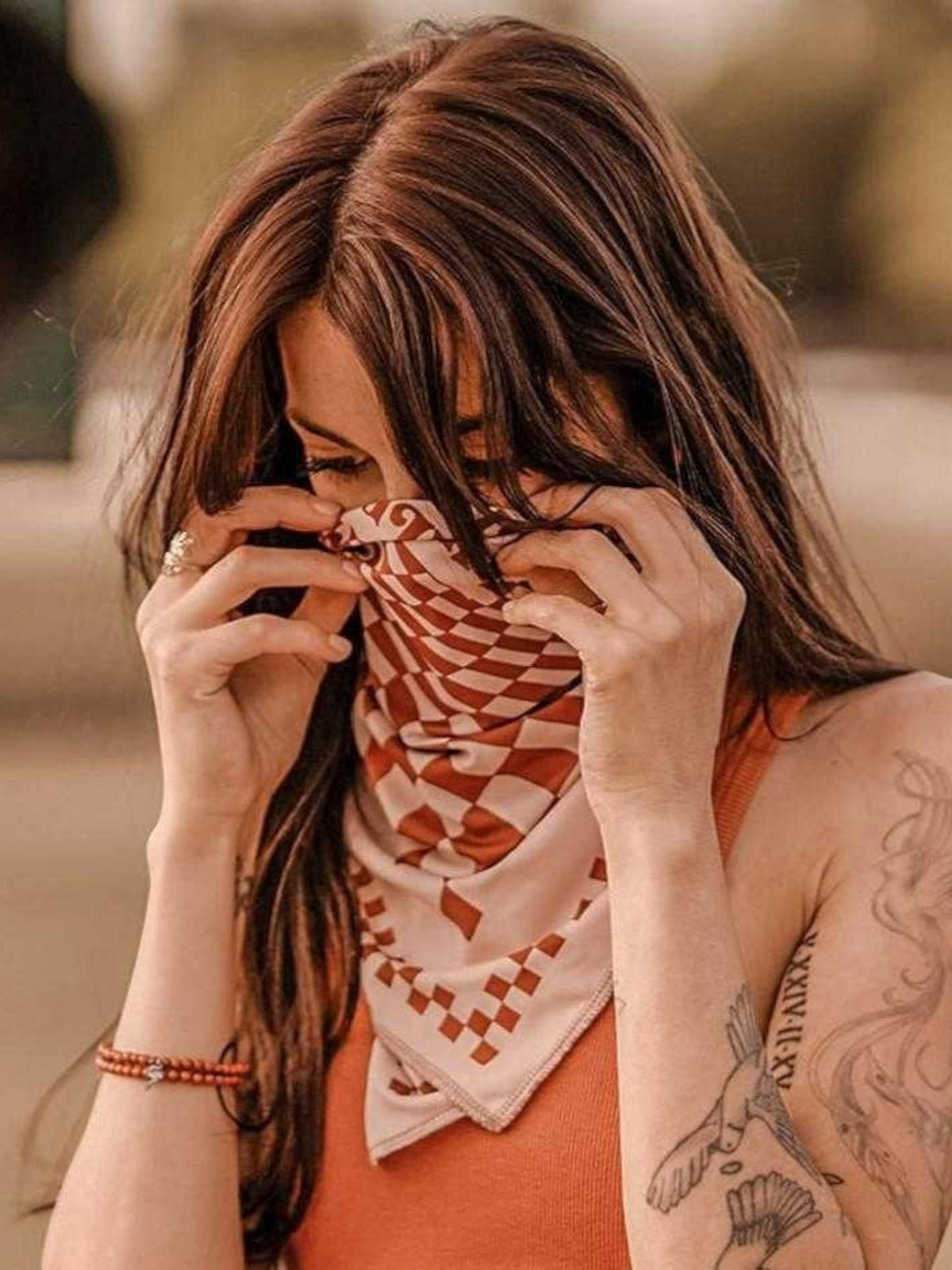 Baffle Haus terracotta and white psychedelic checkerboard scarf worn as a face covering by a woman