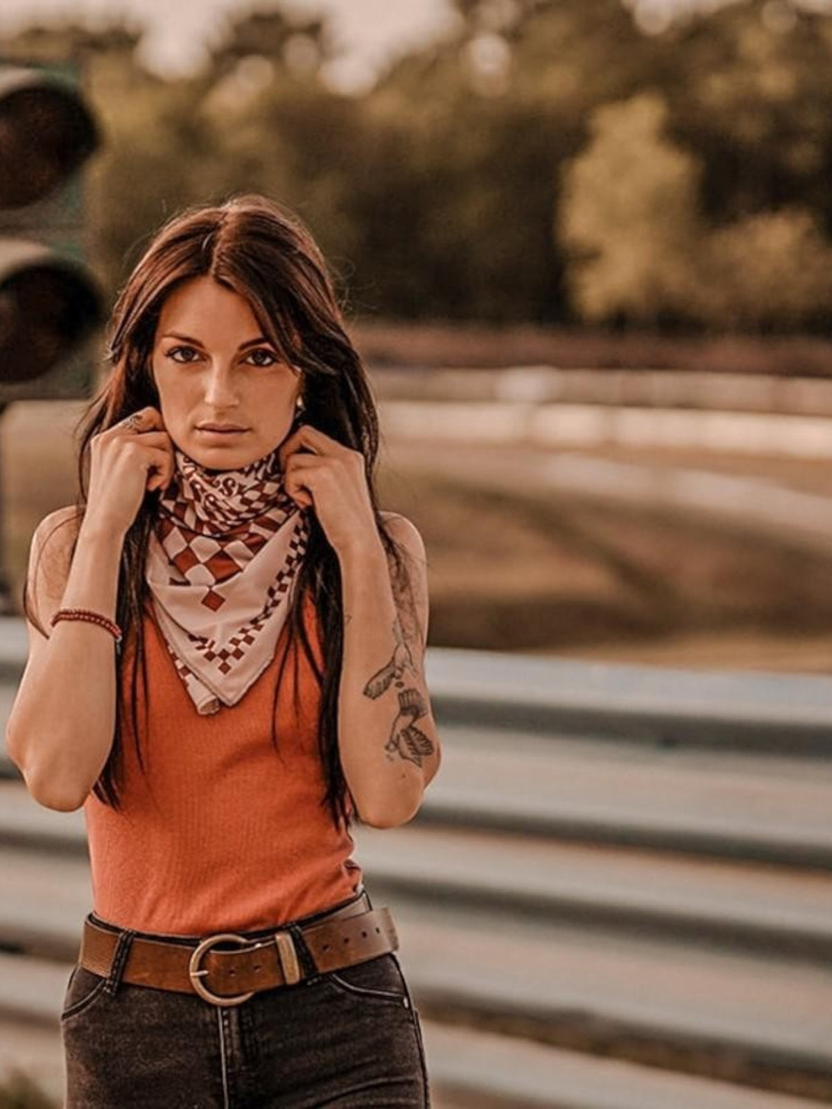 Baffle Haus Petrol Junkies scarf in terracotta with a vintage checkerboard pattern worn by a woman at a racetrack