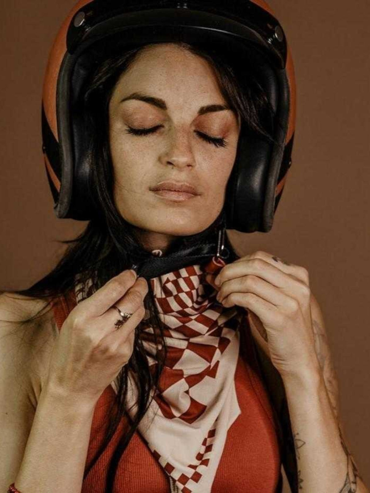 Baffle Haus Petrol Junkies scarf in terracotta and cream checkerboard pattern worn by a woman with a motorcycle helmet