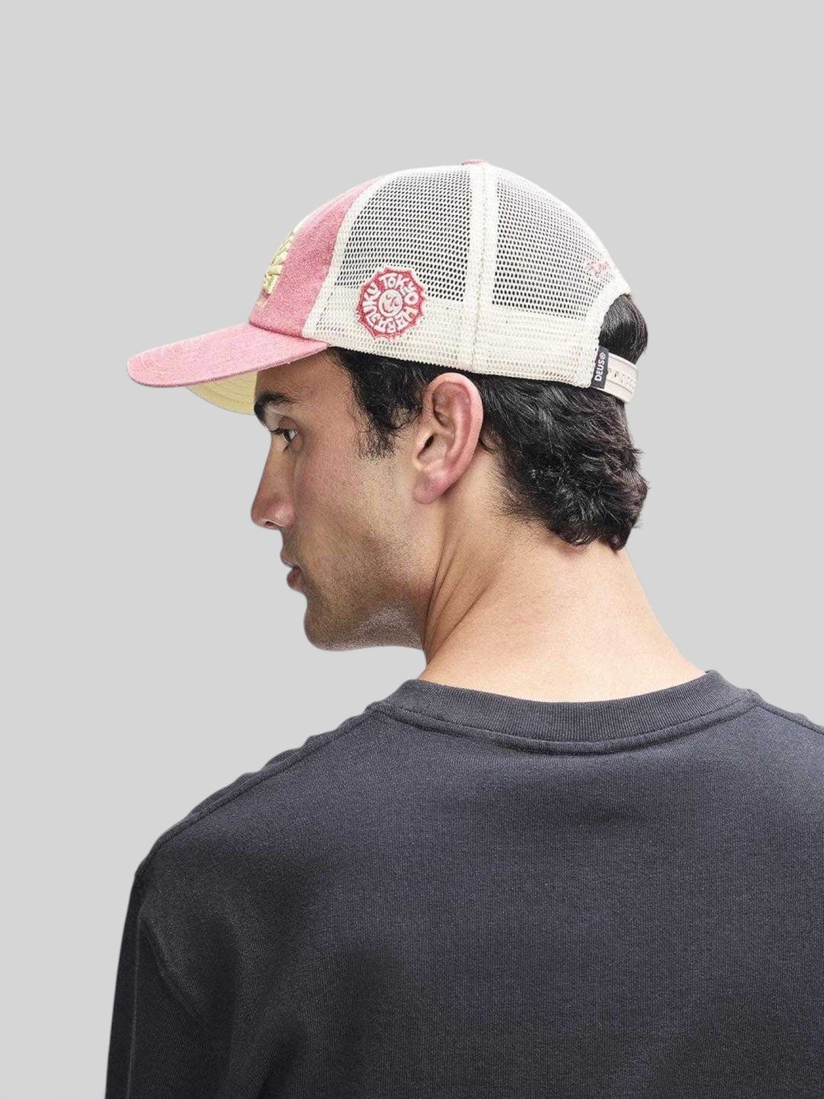 Baffle Haus Tokyo Address trucker hat in melon red with white mesh back, worn by a man in profile view.