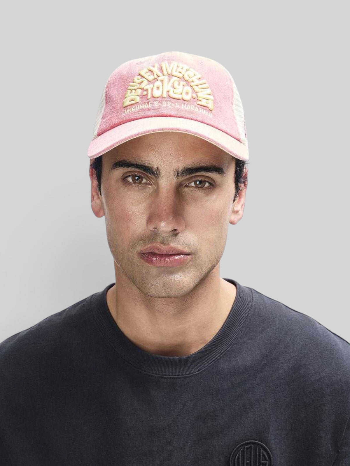 Baffle Haus Tokyo Address trucker hat in melon red with yellow embroidery, contrast stitching, and mesh back.
