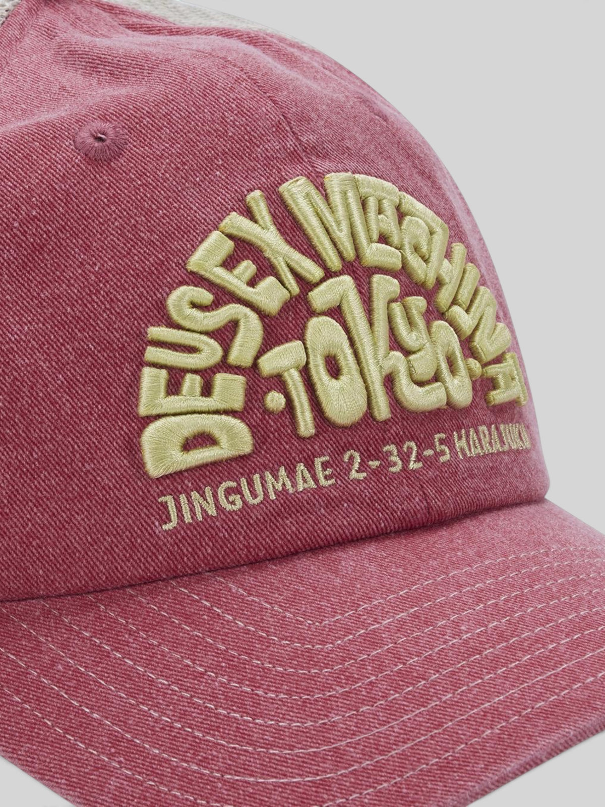 Baffle Haus Tokyo Address trucker hat in melon red with heavy enzyme wash, contrast stitching, and yellow embroidery.