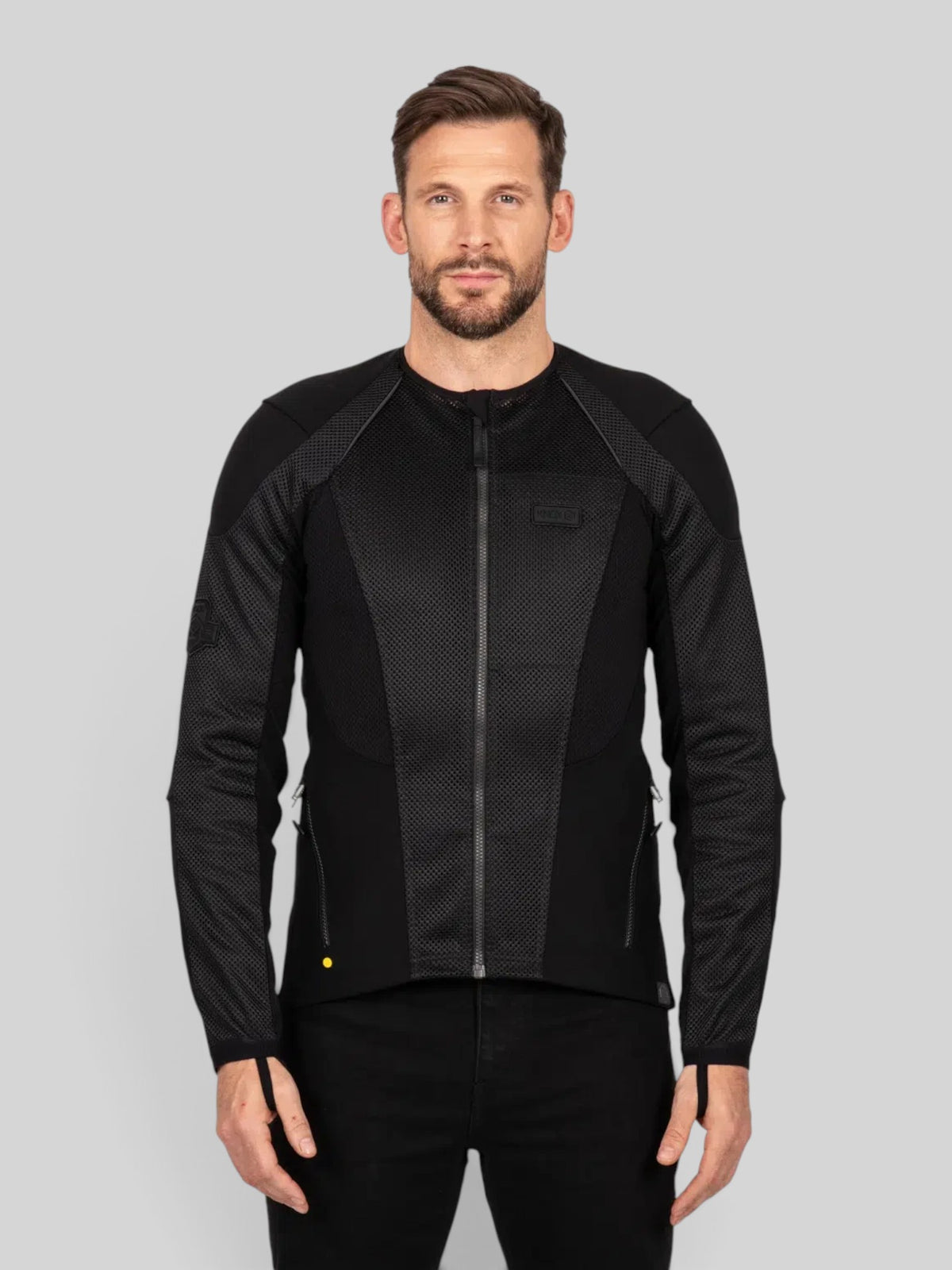 A man wearing a black Baffle Haus Urbane Pro MK3 mesh motorcycle jacket with protective panels.