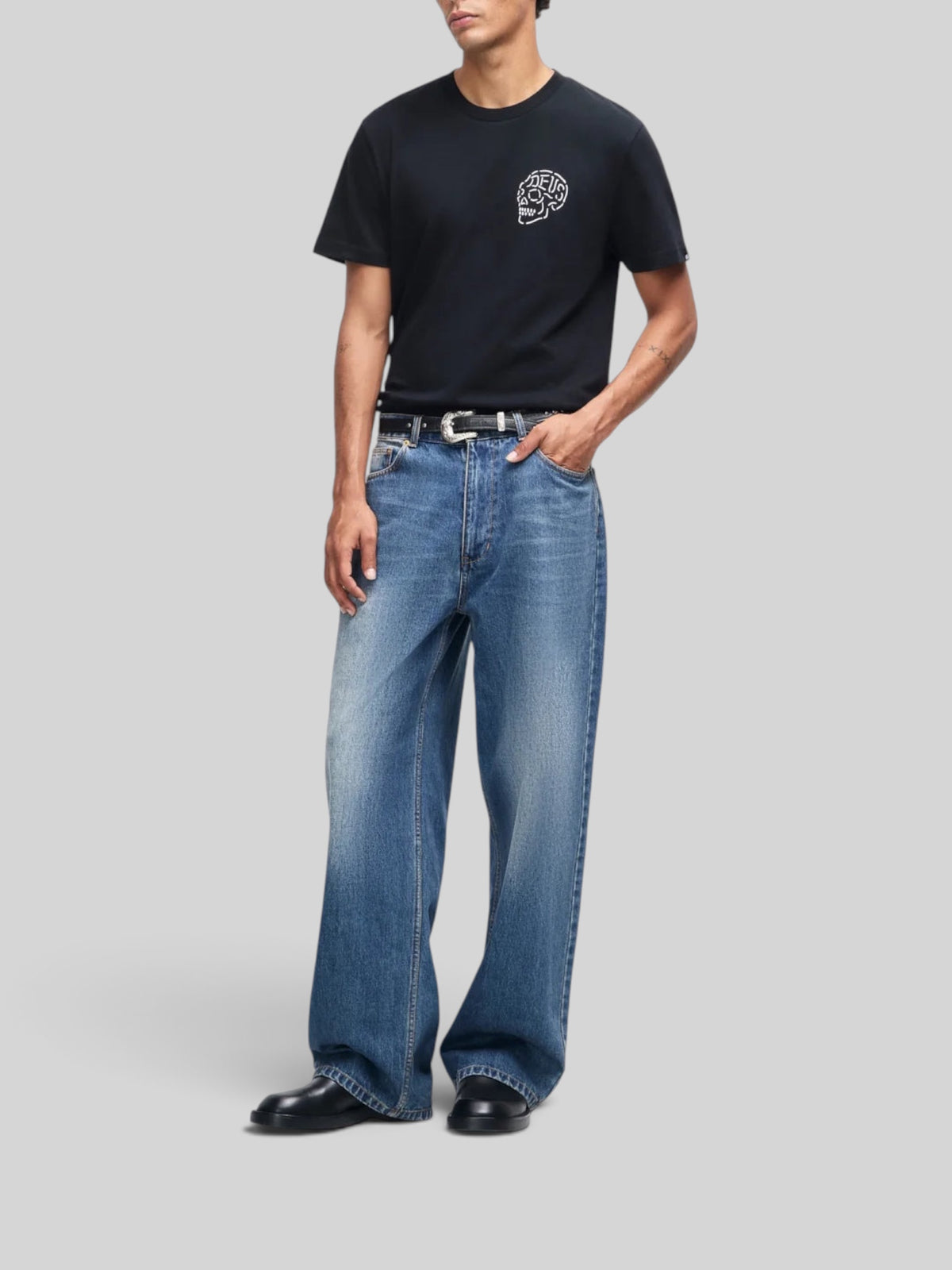 Baffle Haus Venice Skull Tee in black organic cotton with chest graphic, worn by a model with blue denim jeans