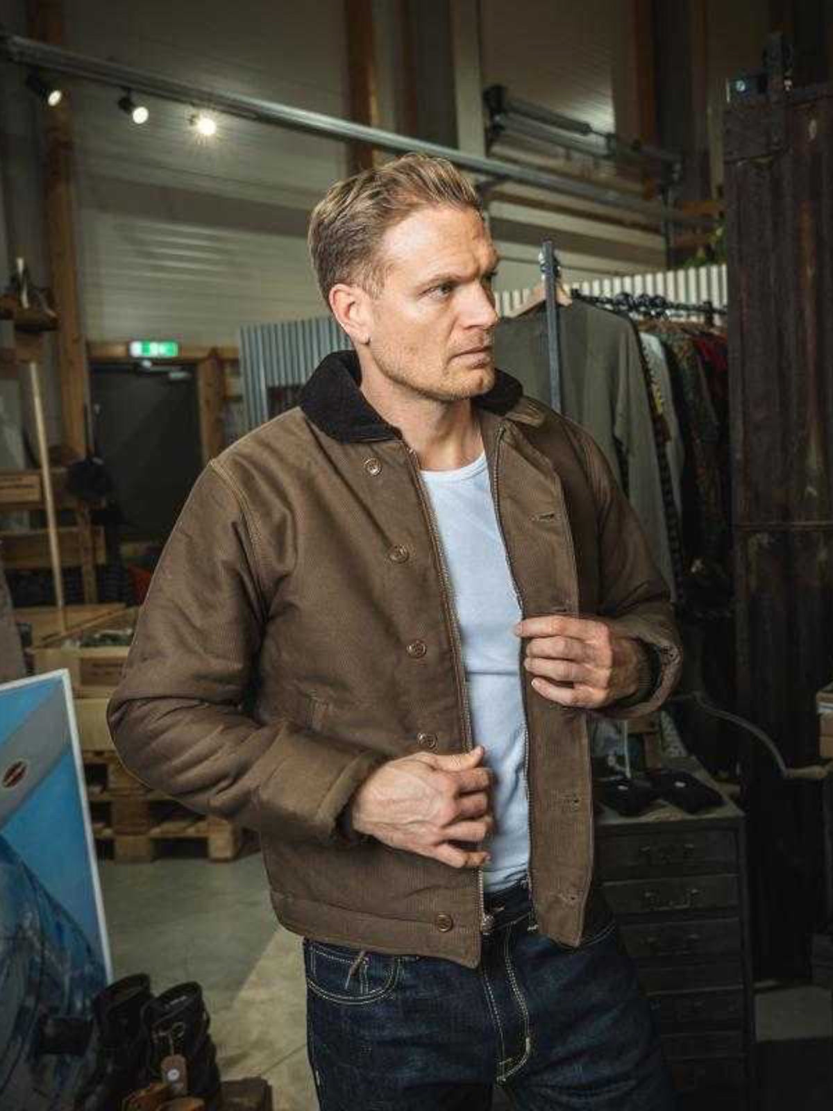 Baffle Haus 1944 N1 Deck Jacket in waxed khaki cotton with wool lining, worn by a man in a workshop setting.