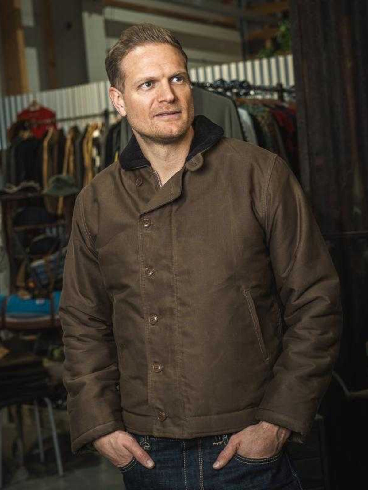 Baffle Haus 1944 N1 Deck Jacket in waxed khaki cotton with a wool-lined stand-up collar worn by a man in a workshop.