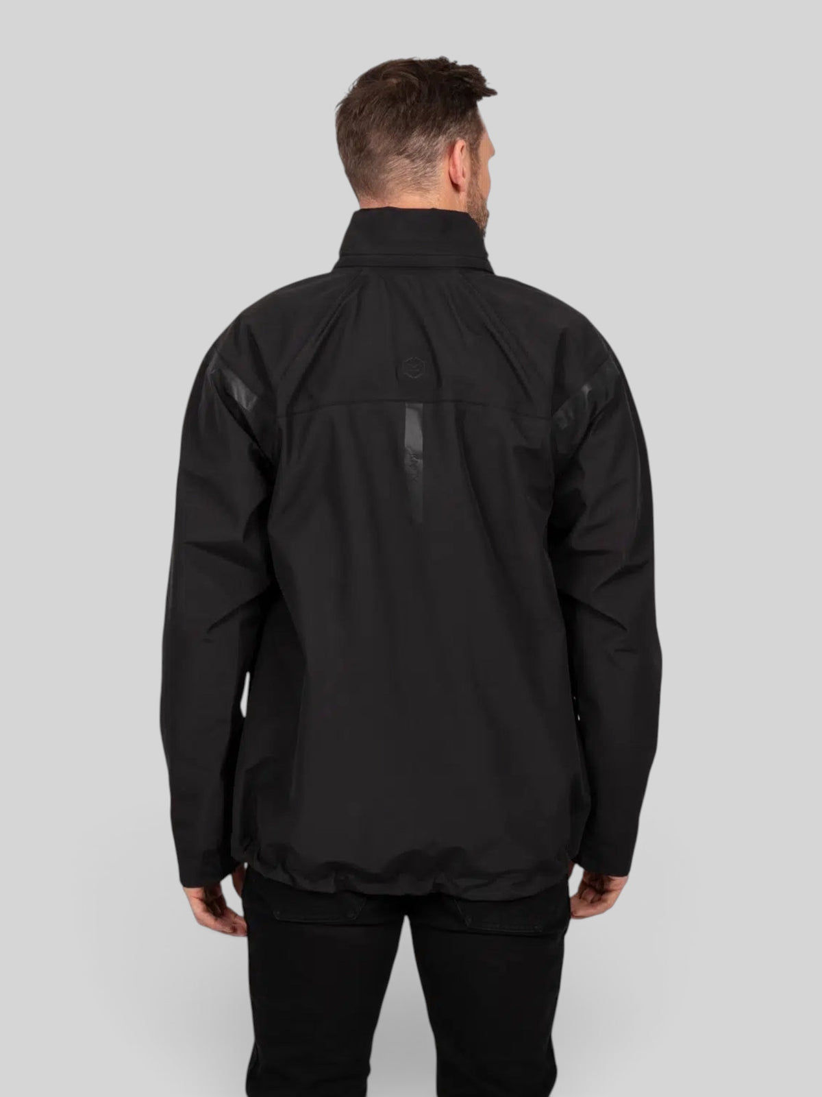 Back view of a man wearing the black Baffle Haus Welbeck Waterproof Overjacket MK2 with reflective detailing.