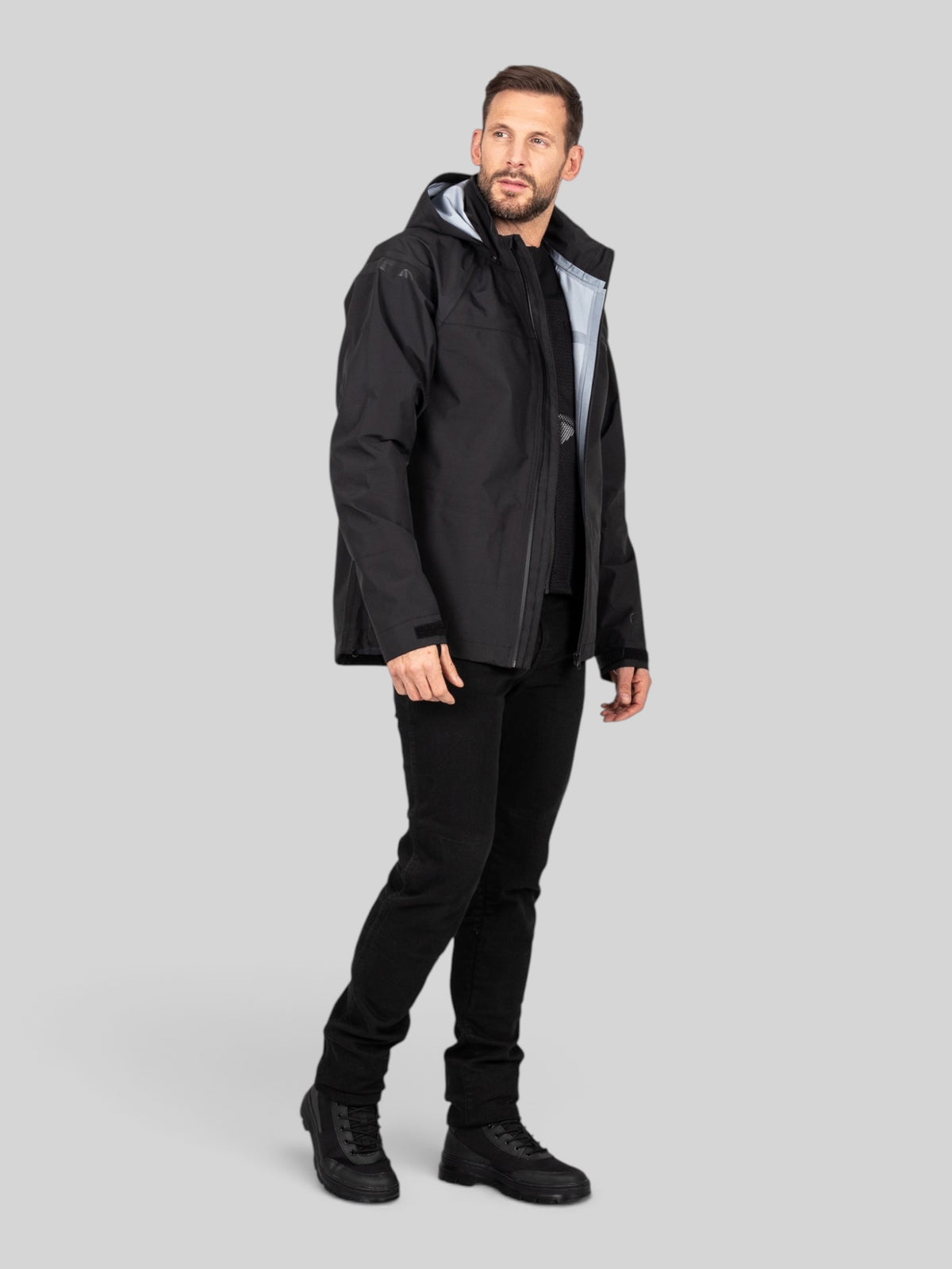 Baffle Haus Welbeck MK2 waterproof black motorcycle overjacket worn by a man, featuring a concealed hood and cuffs.
