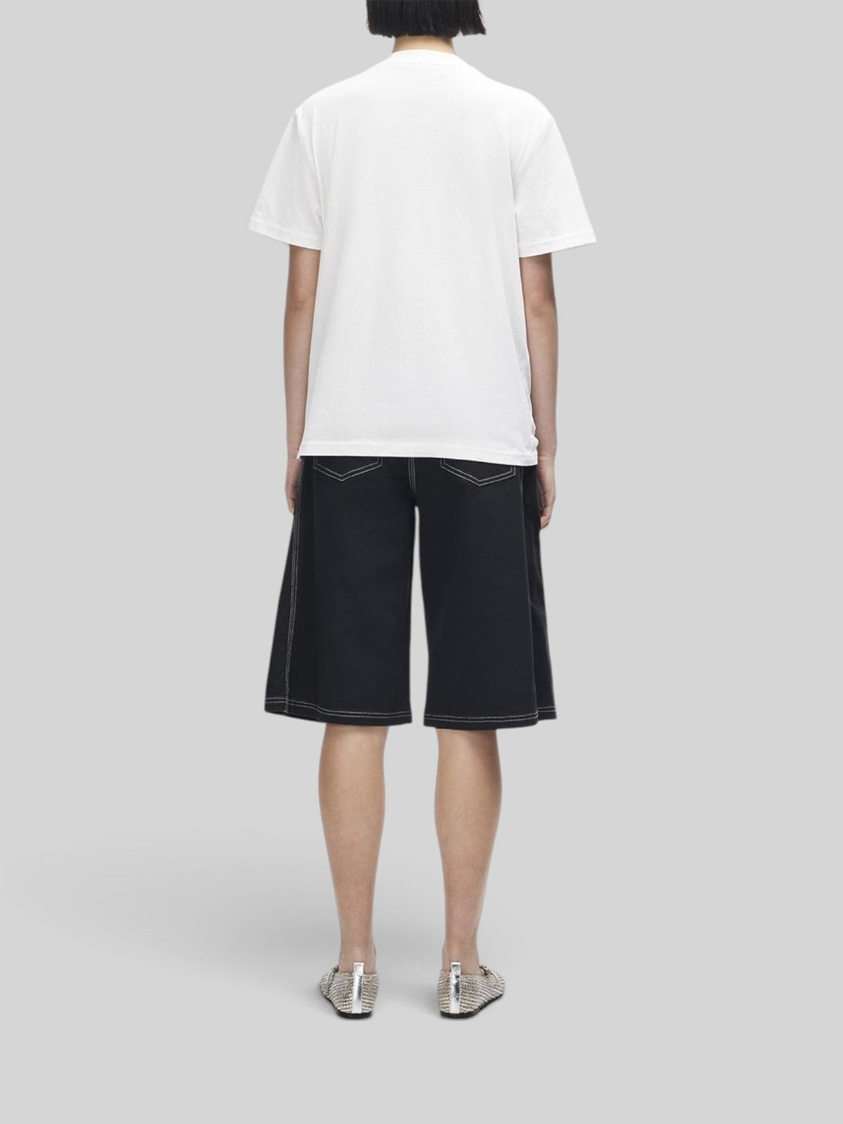 Baffle Haus model wearing a white Deus A110 tee and black shorts with contrast stitching, back view.