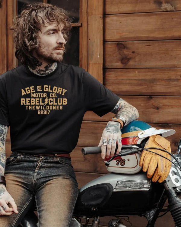 Baffle Haus Wild Ones black cotton t-shirt with vintage motorcycle club graphic worn by a tattooed man on a bike